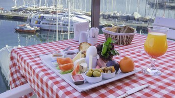 Een tafel met een geruit tafelkleed, een glas sinaasappelsap en diverse soorten eten, waaronder kaas, olijven en brood.