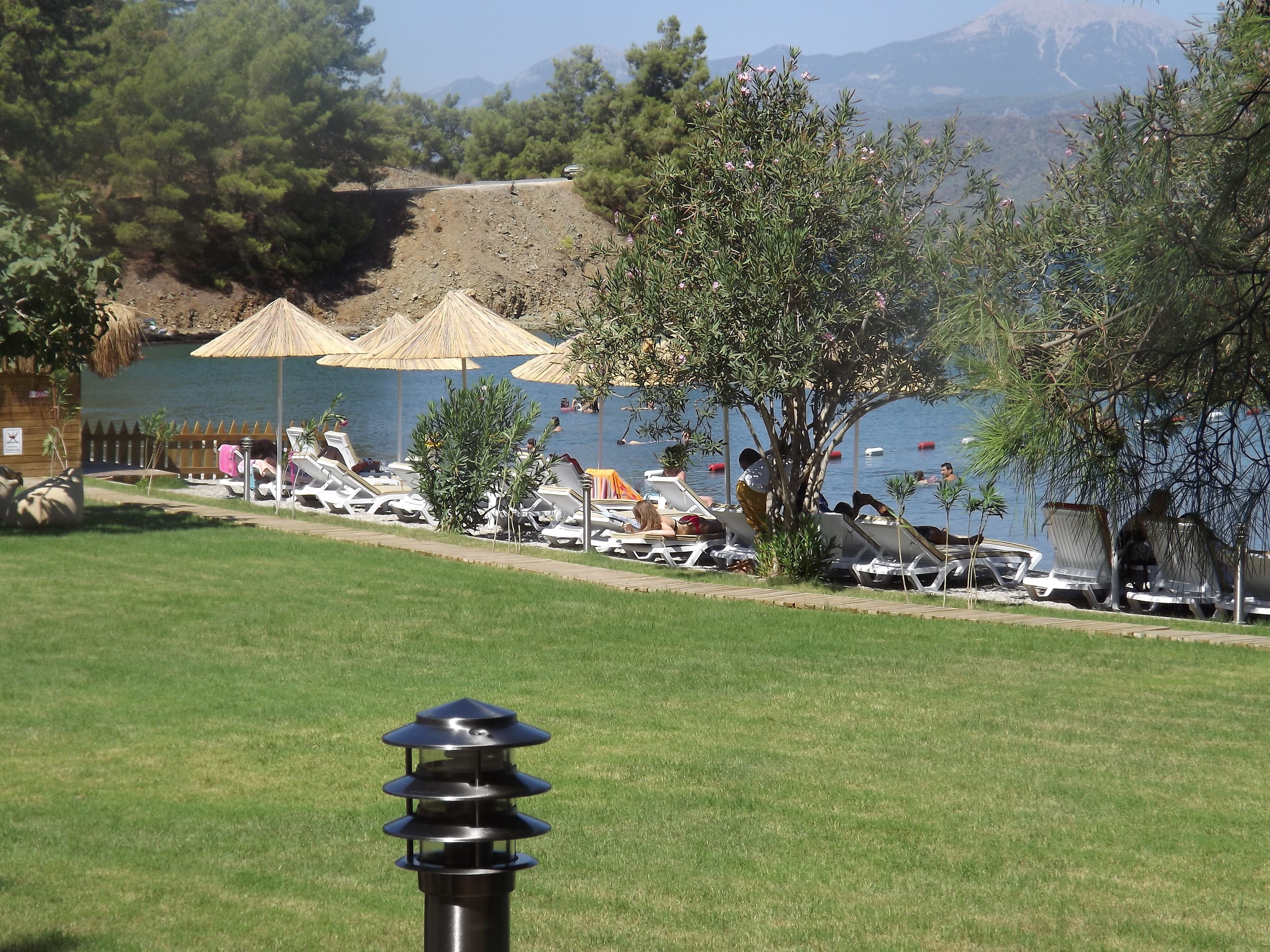 Zona junto a la piscina con sillones de descanso, sombrillas y vistas a un lago y montañas.