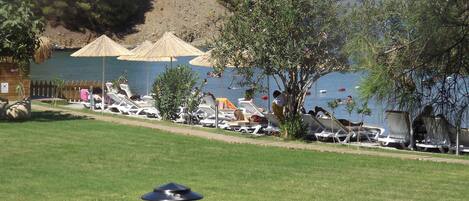 Zona junto a la piscina con sillones de descanso, sombrillas y vistas a un lago y montañas.