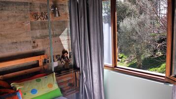 Quarto de criança com cabeceira de madeira, janela com vista para árvores e um balanço pendurado.