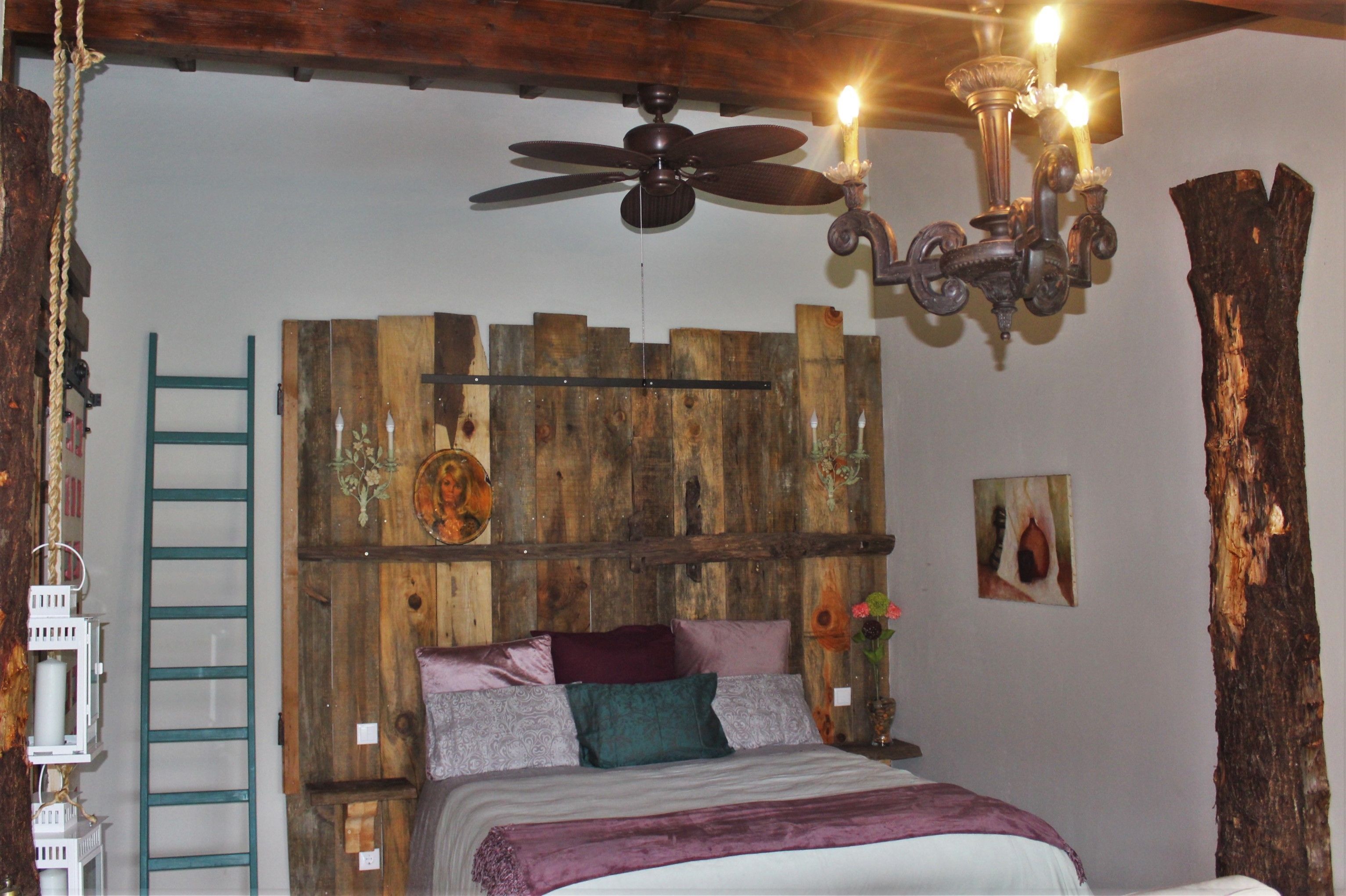 Een slaapkamer met een houten hoofdeinde, een plafondventilator, een kroonluchter en een ladder tegen de muur.