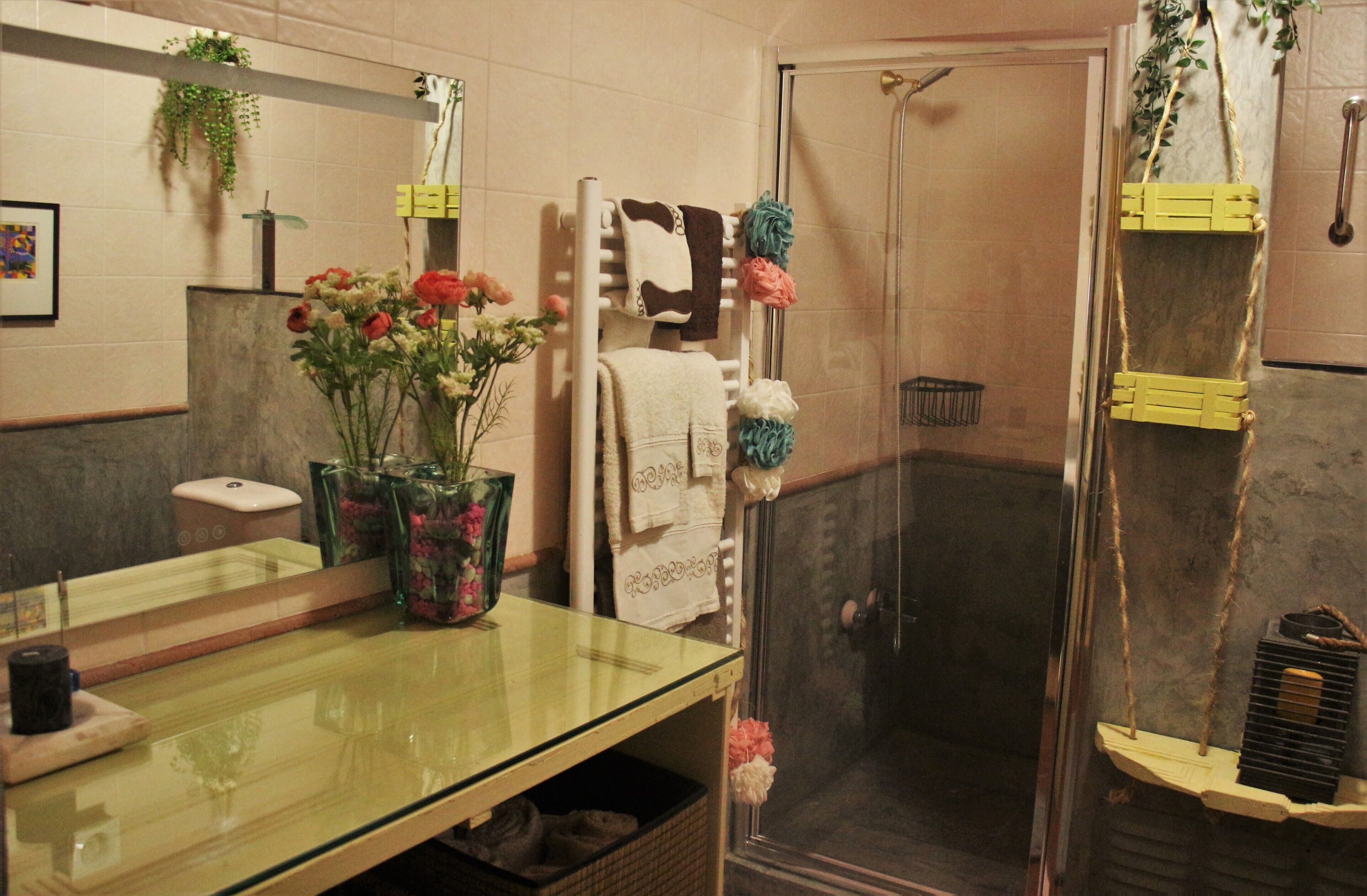 Un baño con cabina de ducha de vidrio, un lavabo con espejo, un perchero con varias toallas y un florero con flores.