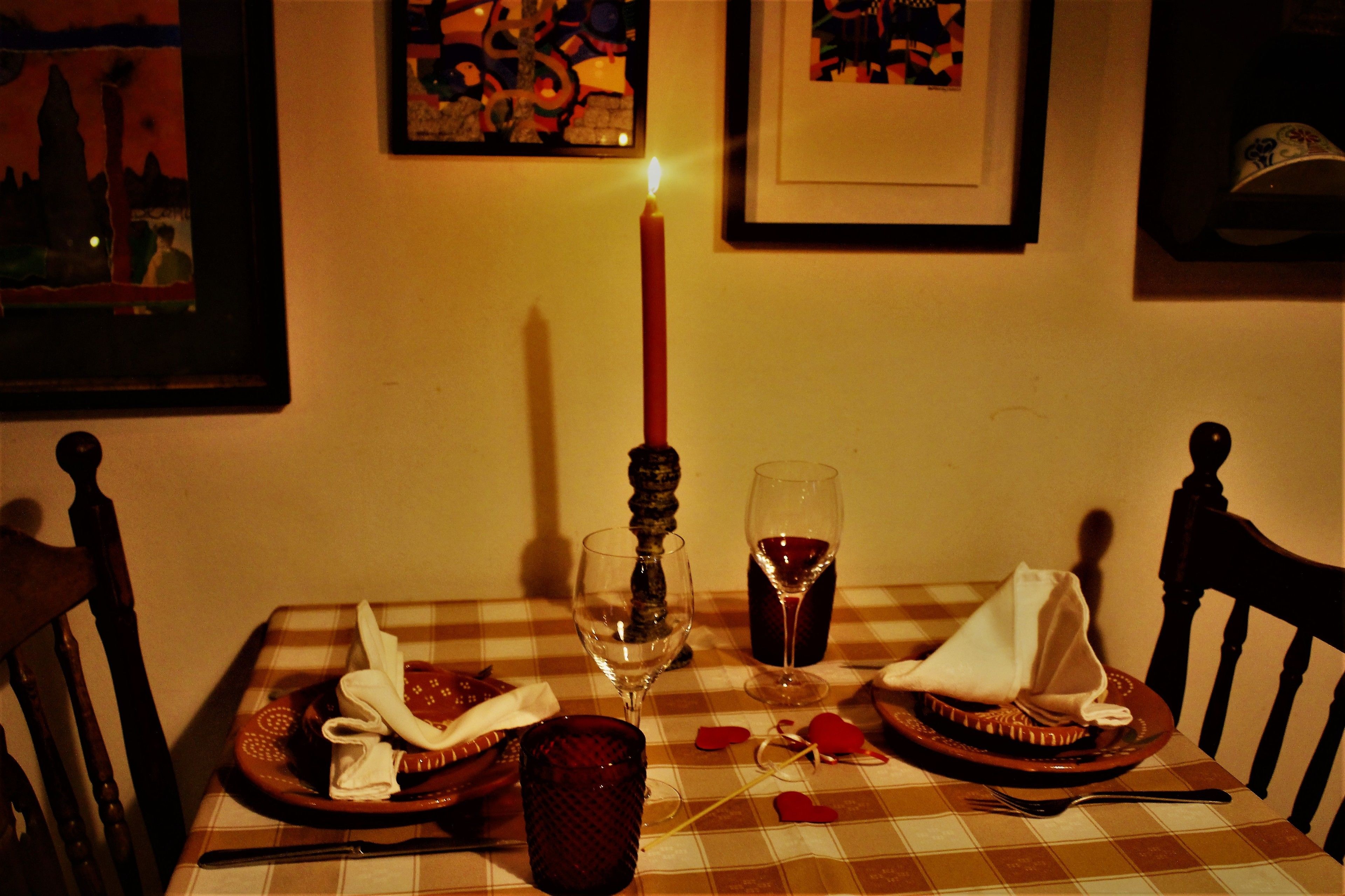 A dining table with a candle, wine glasses, and plates set for two.