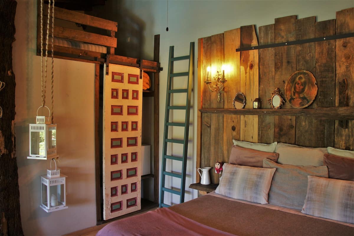 Ein rustikales Schlafzimmer mit einem Holzkopfteil, einer Leiter und einem Bett mit vielen Kissen.