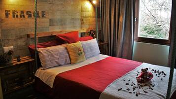 Una cama con ropa de cama roja, un cabecero de madera y una ventana con vistas a árboles.