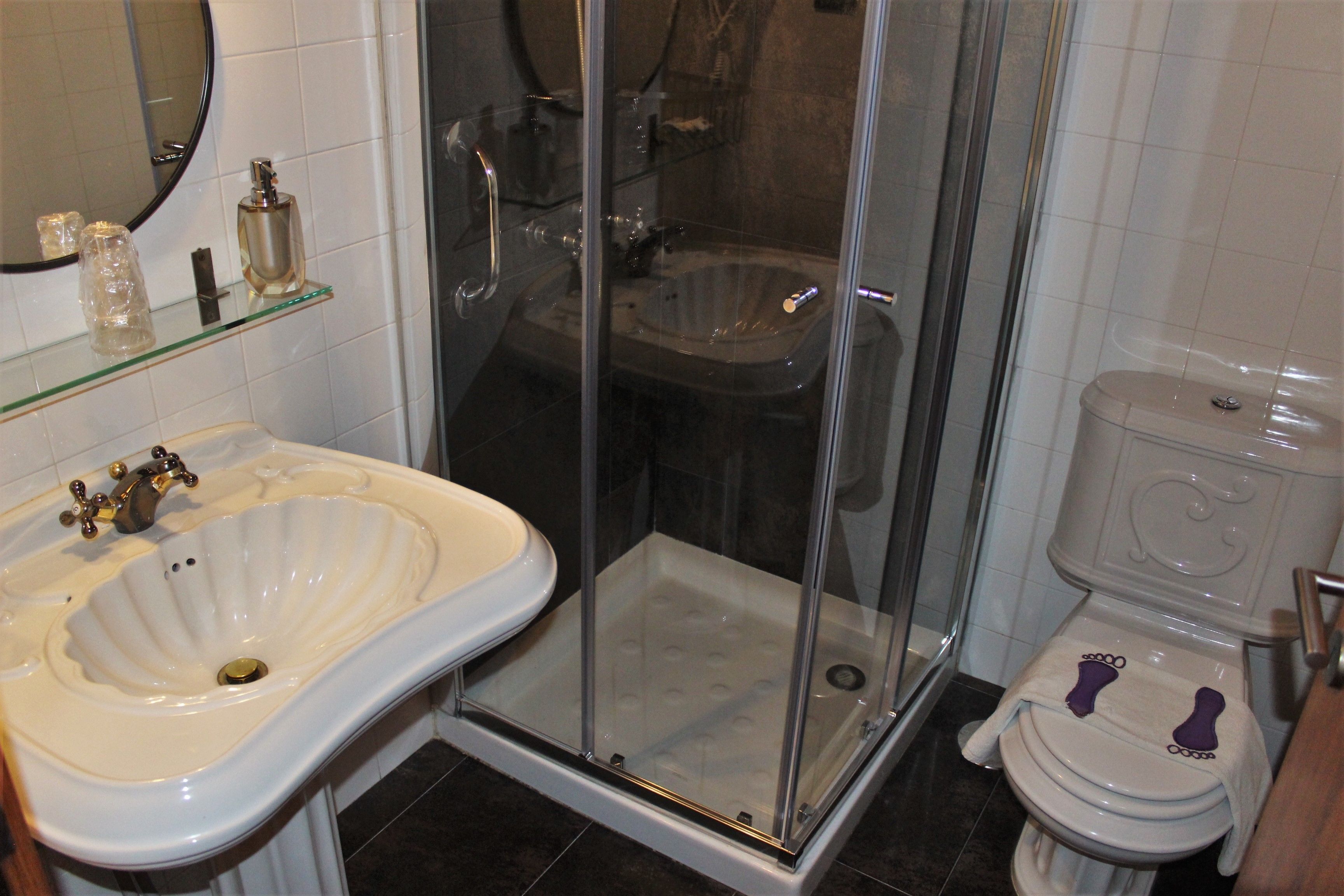A bathroom with a glass-enclosed shower, a pedestal sink, and a toilet with a footrest.