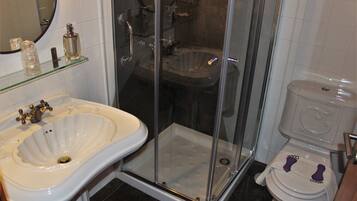 A bathroom with a glass-enclosed shower, a pedestal sink, and a toilet with a footrest.