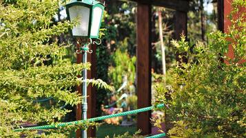 A green street lamp in a garden with a wooden pergola structure in the background.