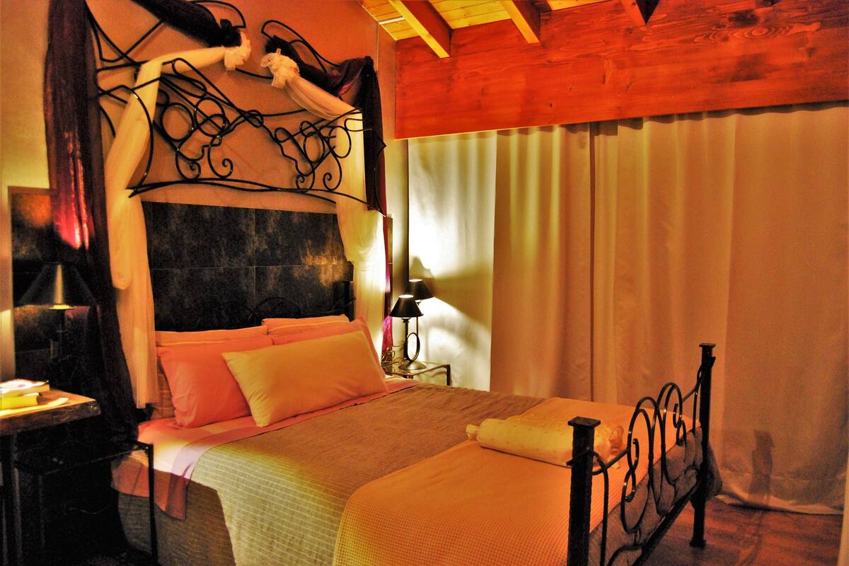 Ein Schlafzimmer mit Bett, Nachttisch, Lampe und Vorhängen.