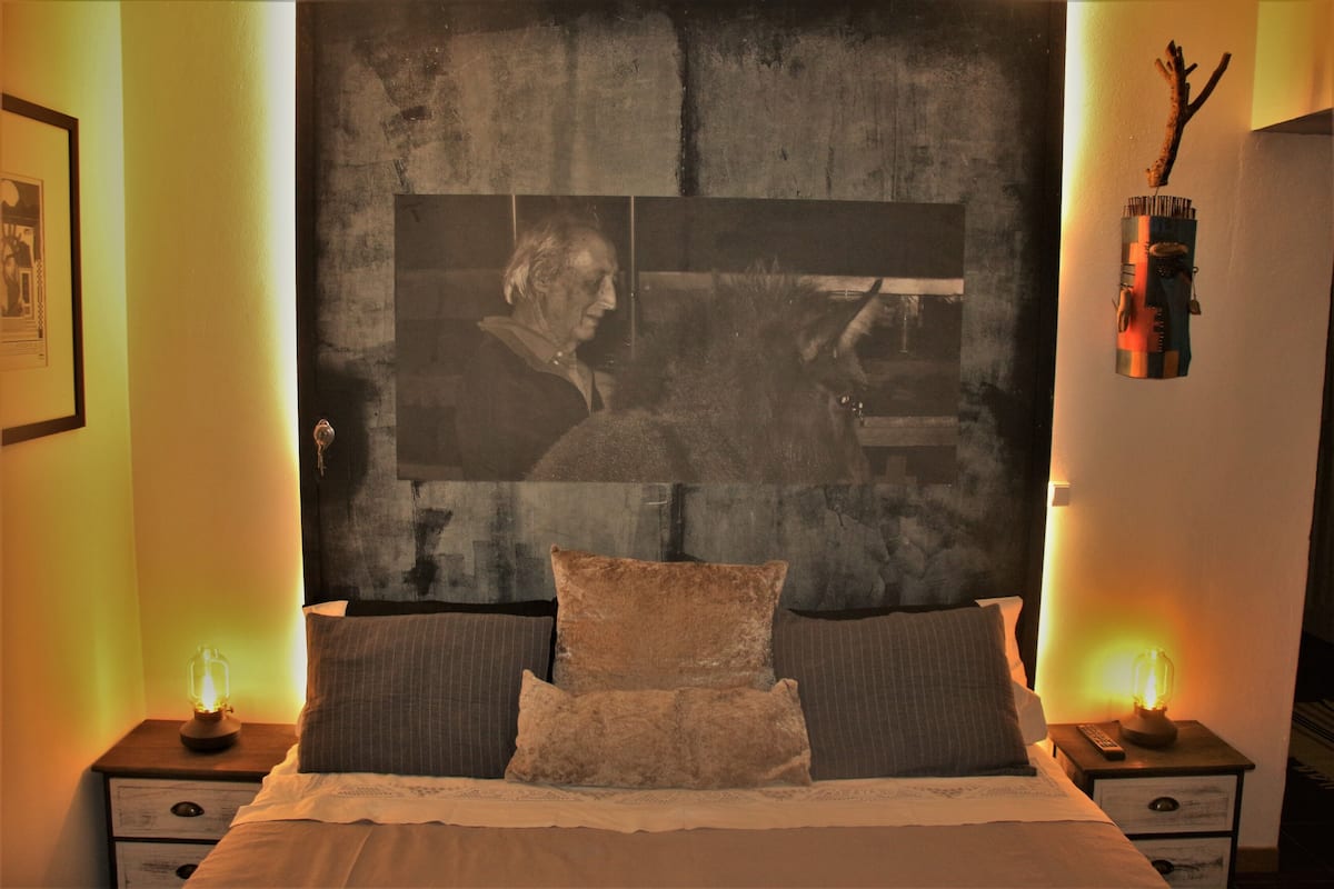 Ein Schlafzimmer mit einem großen Bett, zwei Nachttischen, einem Wandbild und einem Beistelltischchen mit einer Lampe.