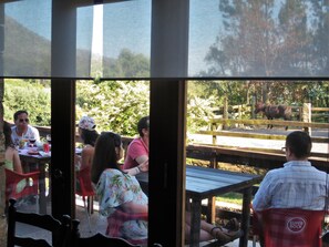 An outdoor seating area with tables and chairs, a wooden deck, and a horse enclosure visible through the window. - Quintinha D' Arga (Caminha)