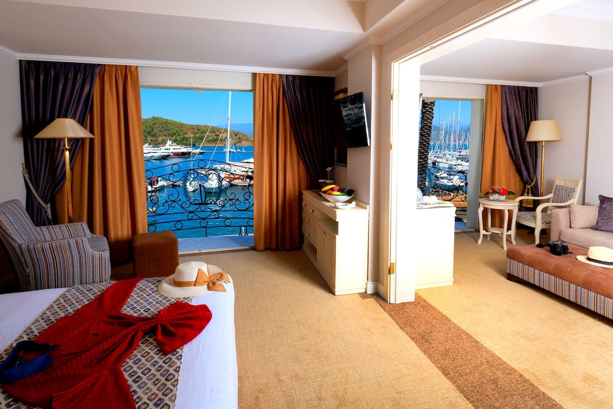 Quarto de hotel com cama, mesa de trabalho, sofá e vista para um cais.