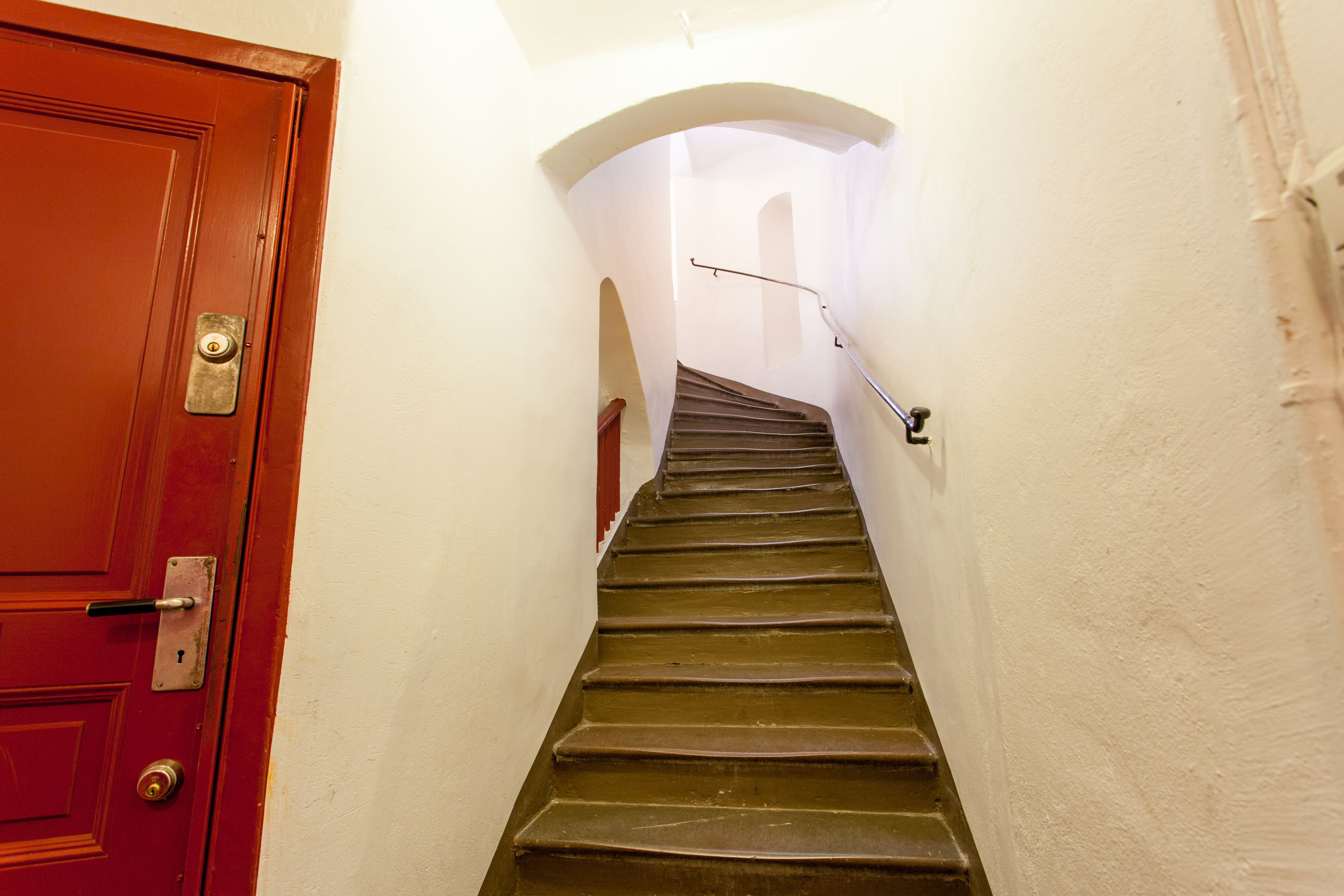 A wooden staircase with a metal handrail, leading to an arched doorway.