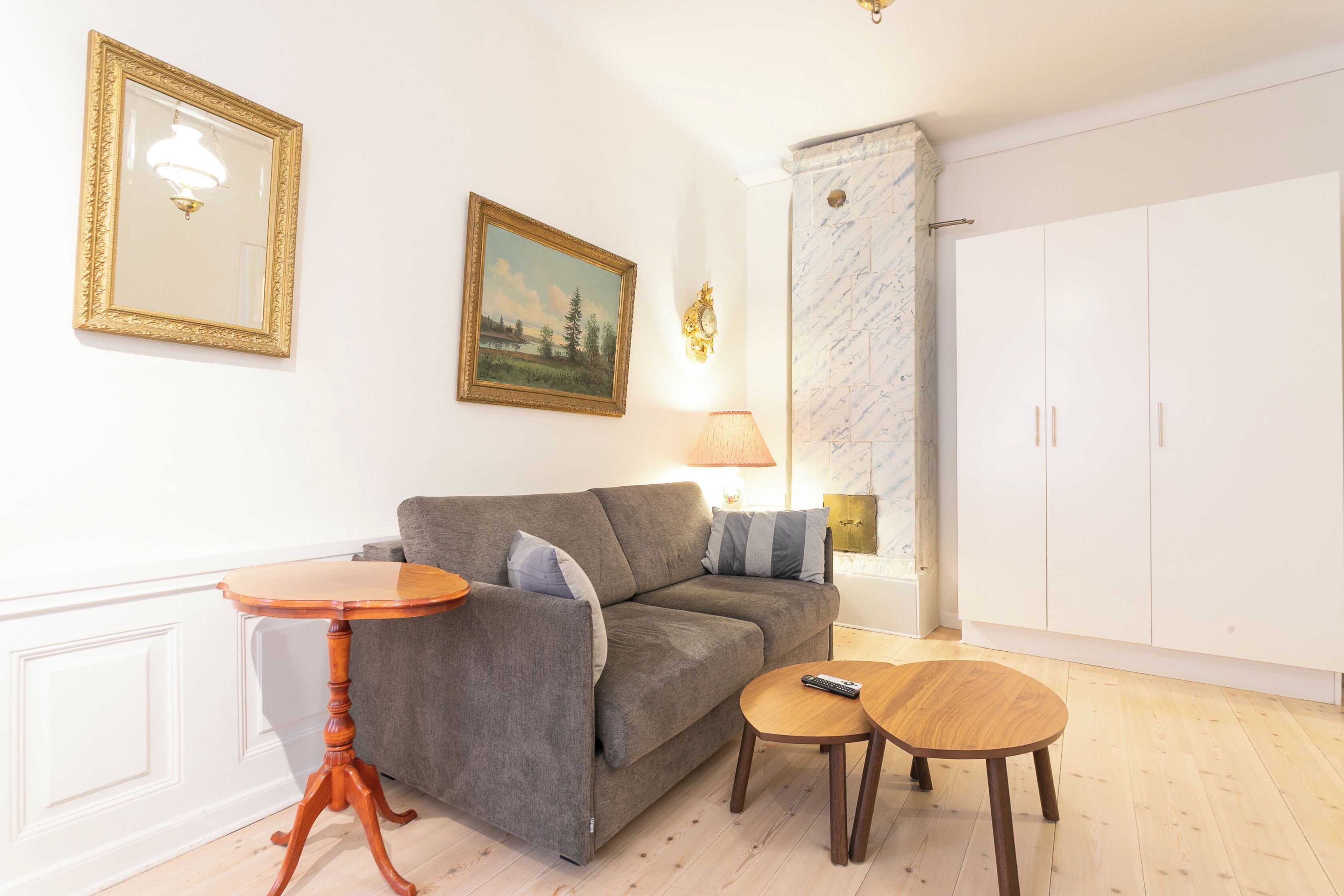 Una sala de estar con un sofá gris, una mesita de madera, una lámpara y un cuadro en la pared.