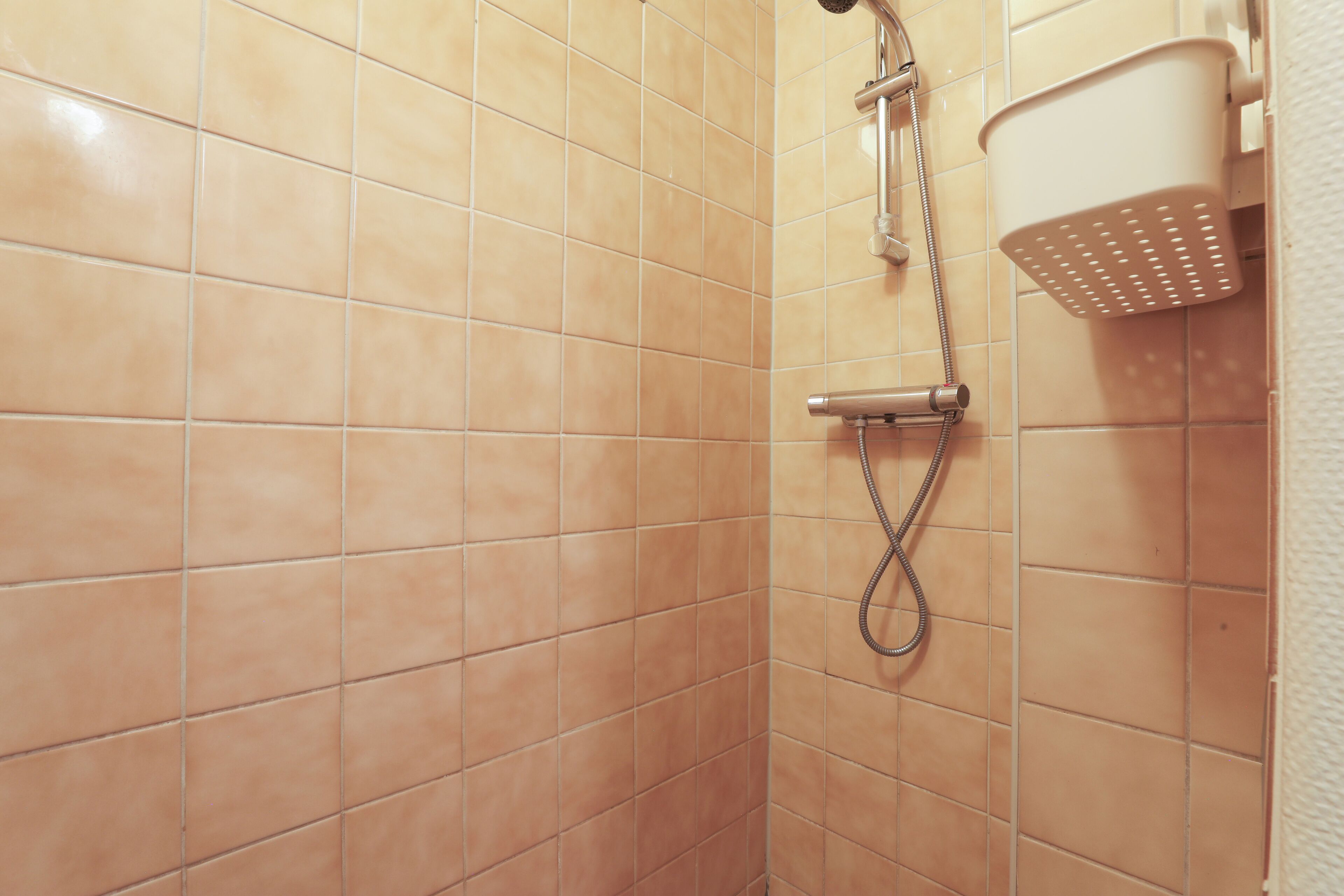 A shower area with beige tiles, a handheld showerhead, and a wall-mounted showerhead.