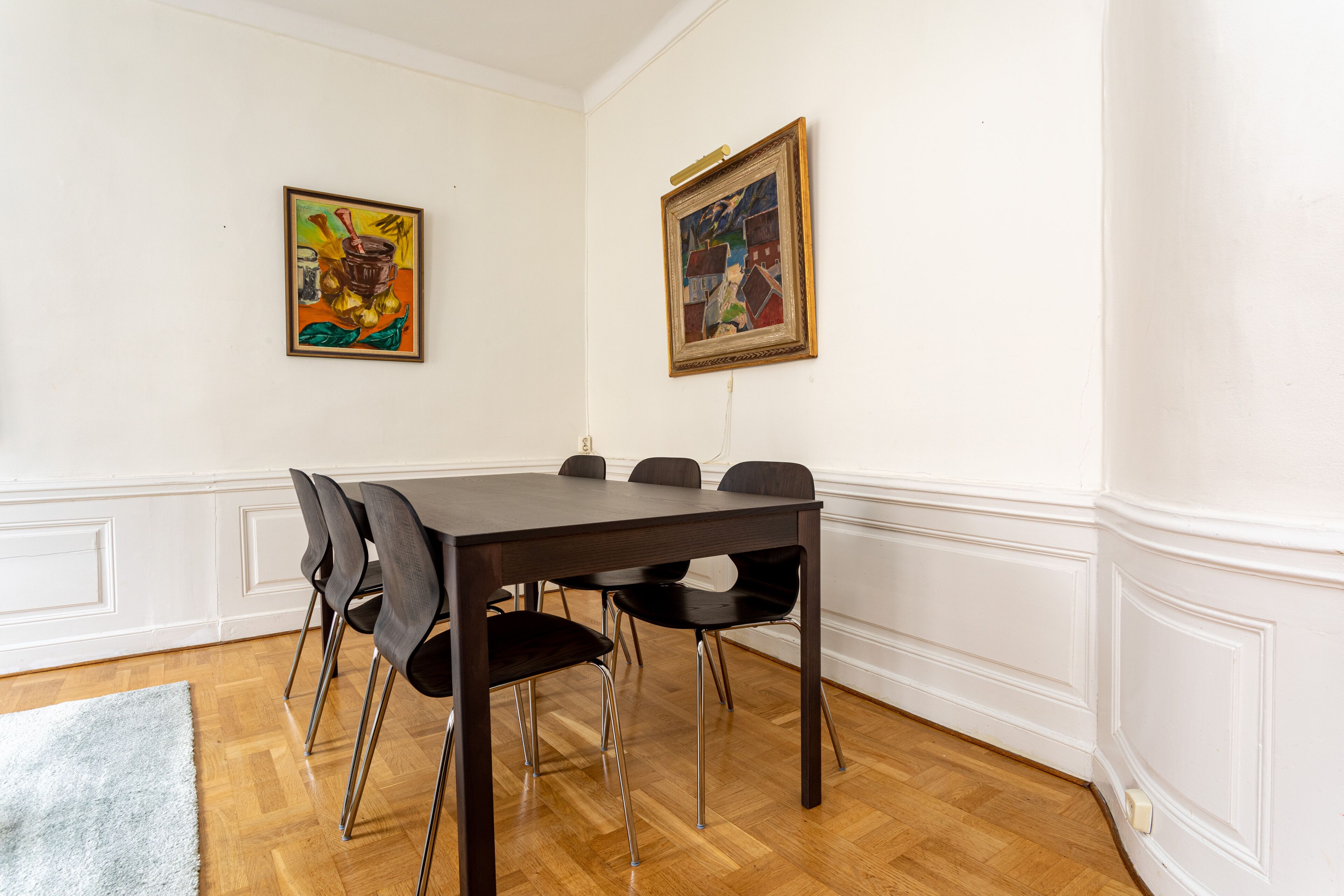 Ein Esszimmer mit Holztisch, sechs Stühlen, weißen Wänden und zwei gerahmten Bildern.