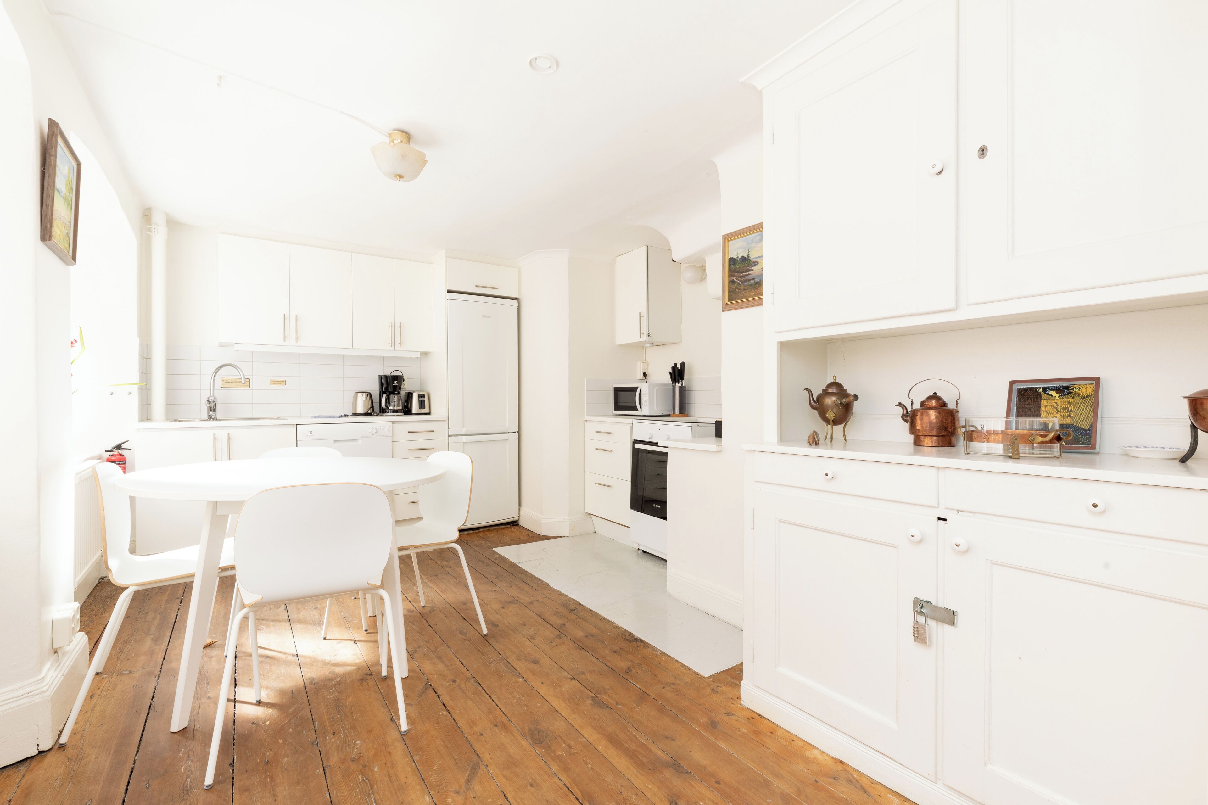 Een moderne keuken met witte kasten, een houten vloer en een eethoek met witte stoelen.