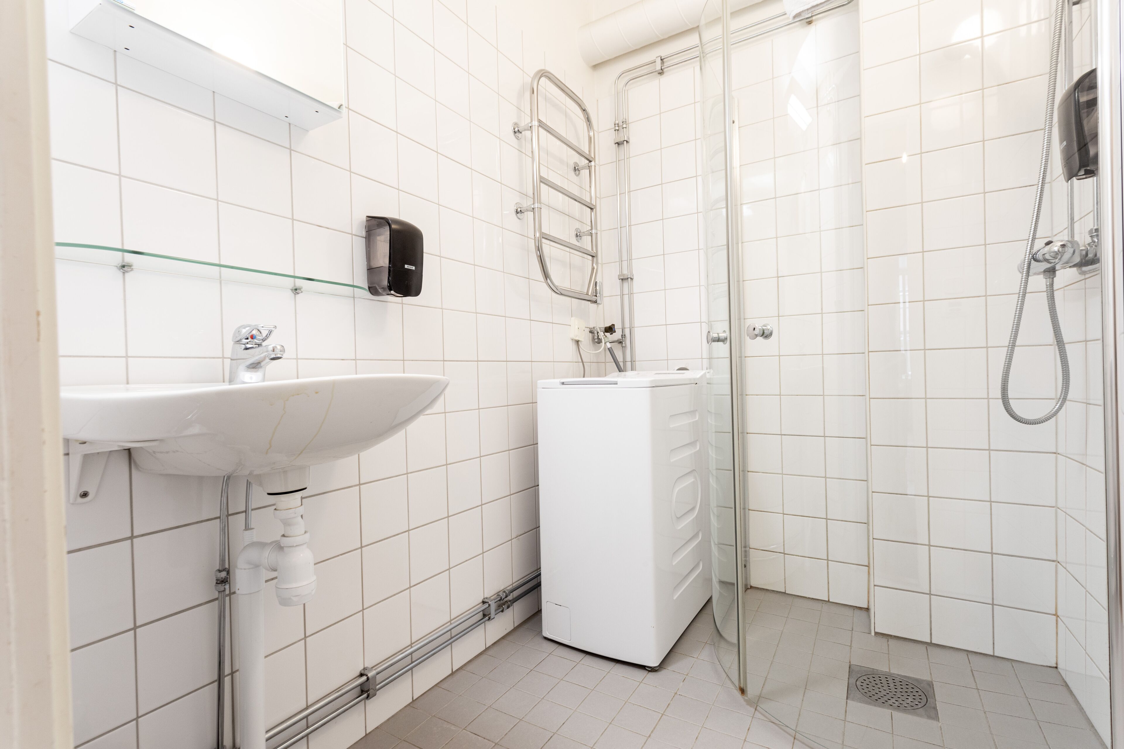 Une salle de bain moderne avec un lavabo blanc, une douche en verre et un lave-linge encastré.
