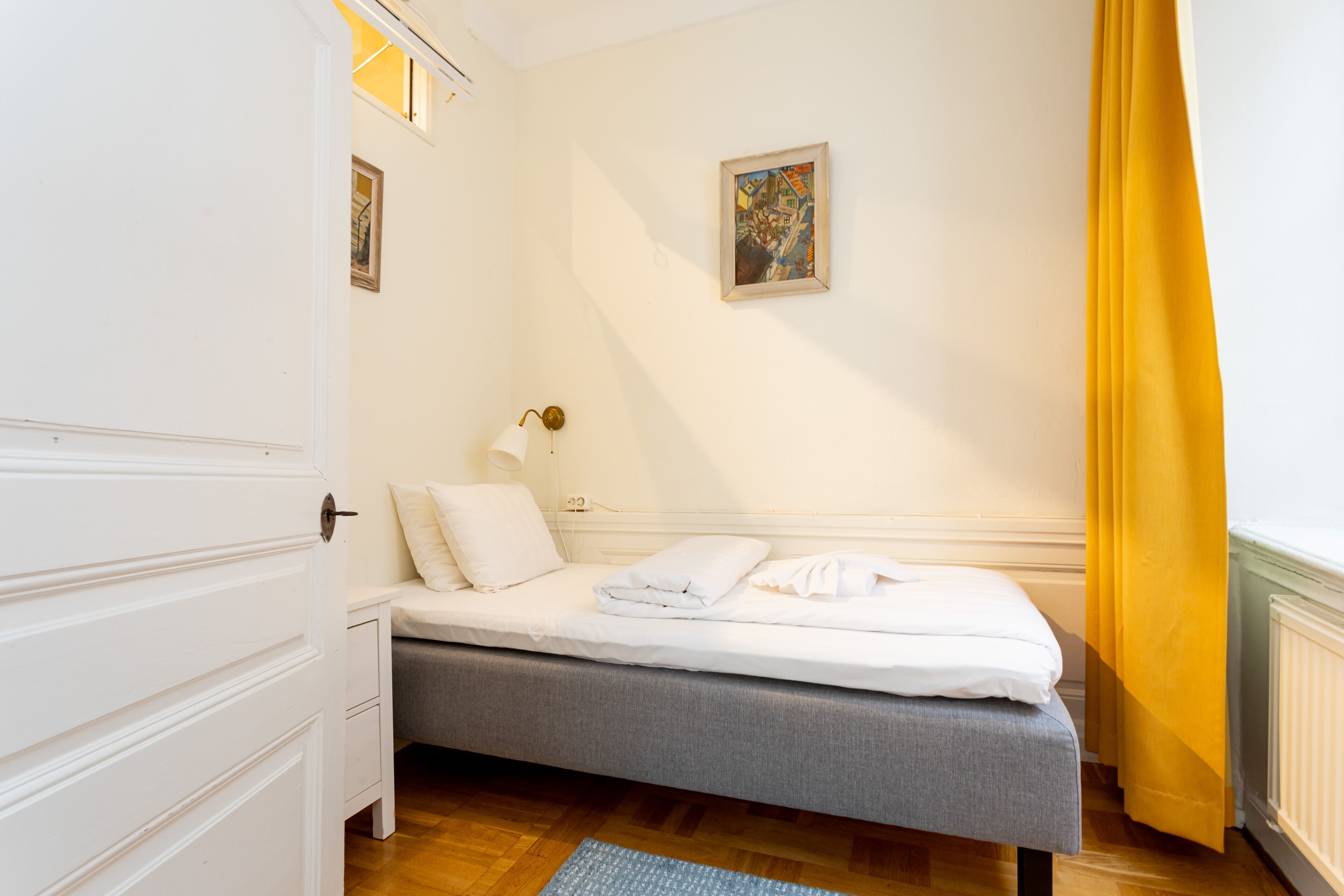 A bedroom with a bed, a bedside table with a lamp, a wardrobe, and a painting on the wall.