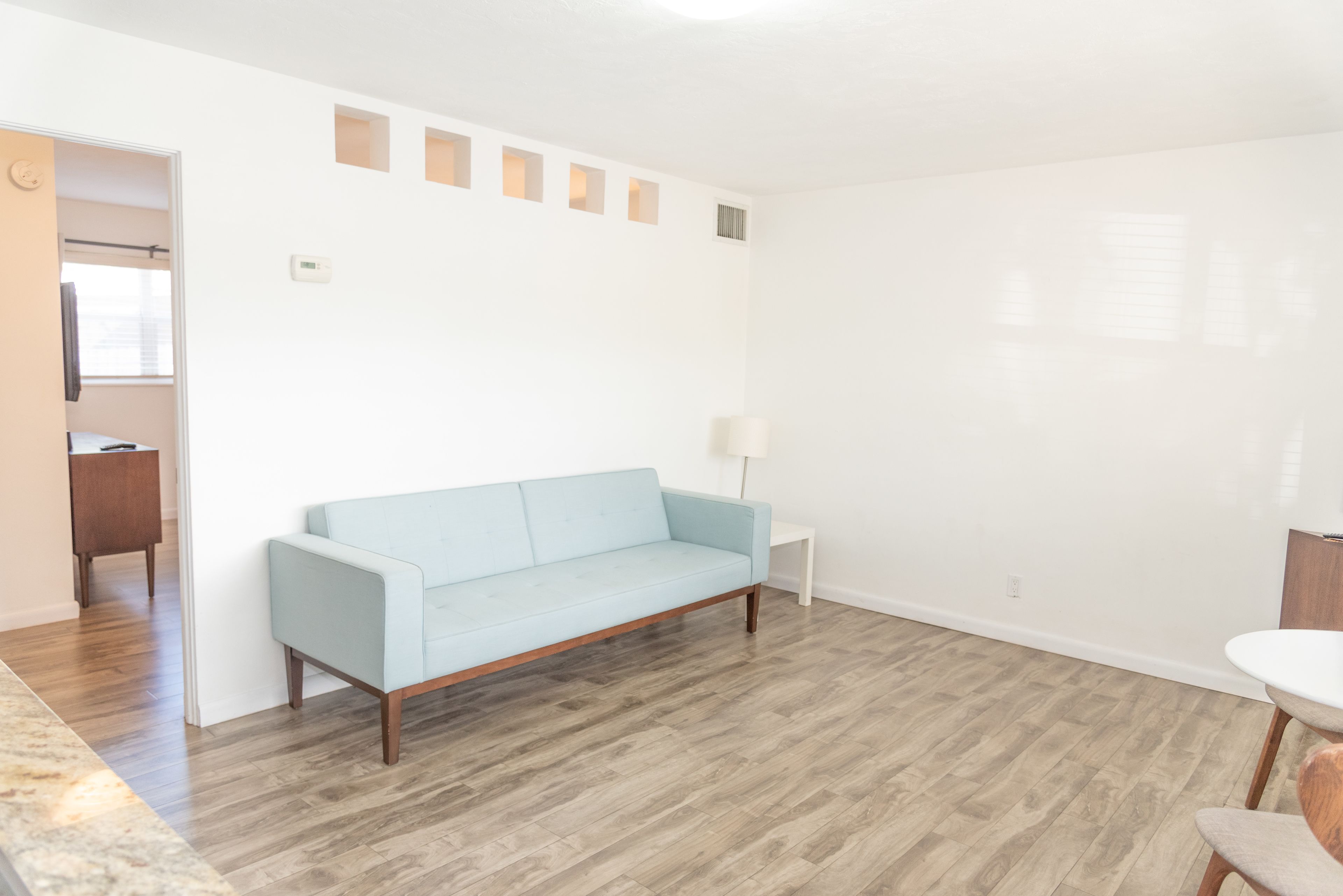 A modern living room with a light blue sofa, a small white side table, and a wooden floor.