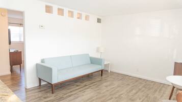 Een moderne woonkamer met een lichtblauwe bank, een klein witte bijzettafeltje en een houten vloer.