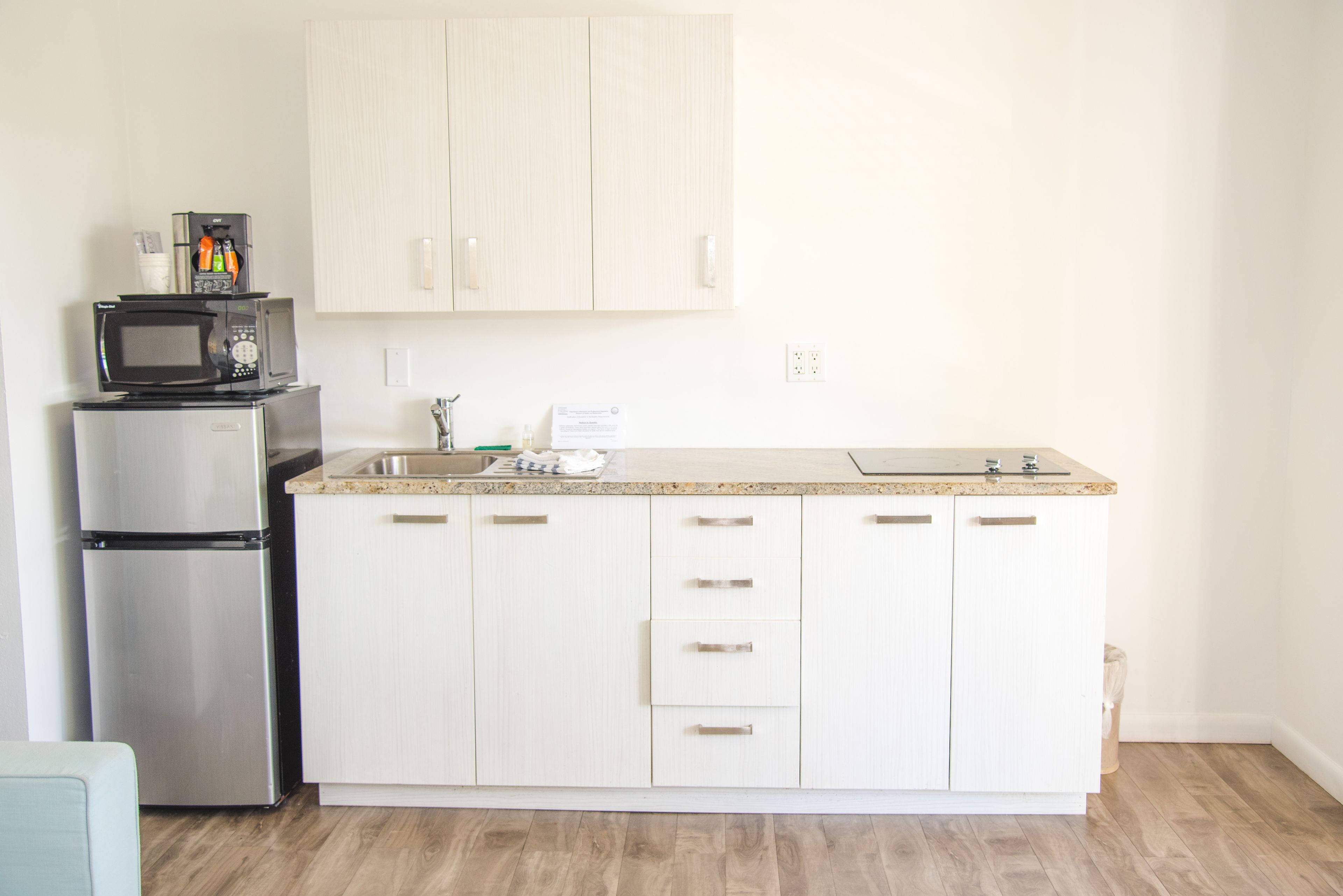 A kitchen with white cabinets, a stainless steel refrigerator, a microwave, and a sink.