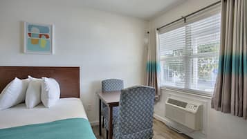 Una habitación de hotel con cama, escritorio, silla, ventana con cortinas y aire acondicionado.