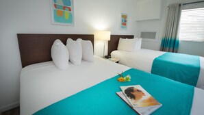 Habitación de hotel con dos camas, una mesita de noche, una lámpara y un ventanal con cortinas.