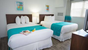 Een hotelkamer met twee bedden, elk voorzien van witte lakens en kussens in teal-kleur. Twee nachtkastjes met lampen, een klein tafeltje met een tijdschrift, en een televisie op een standaard.