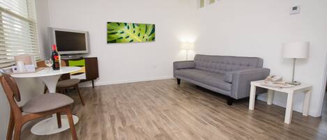 Uma sala de estar moderna com um sofá cinzento, uma mesa de jantar com cadeiras, uma televisão e um quadro na parede.