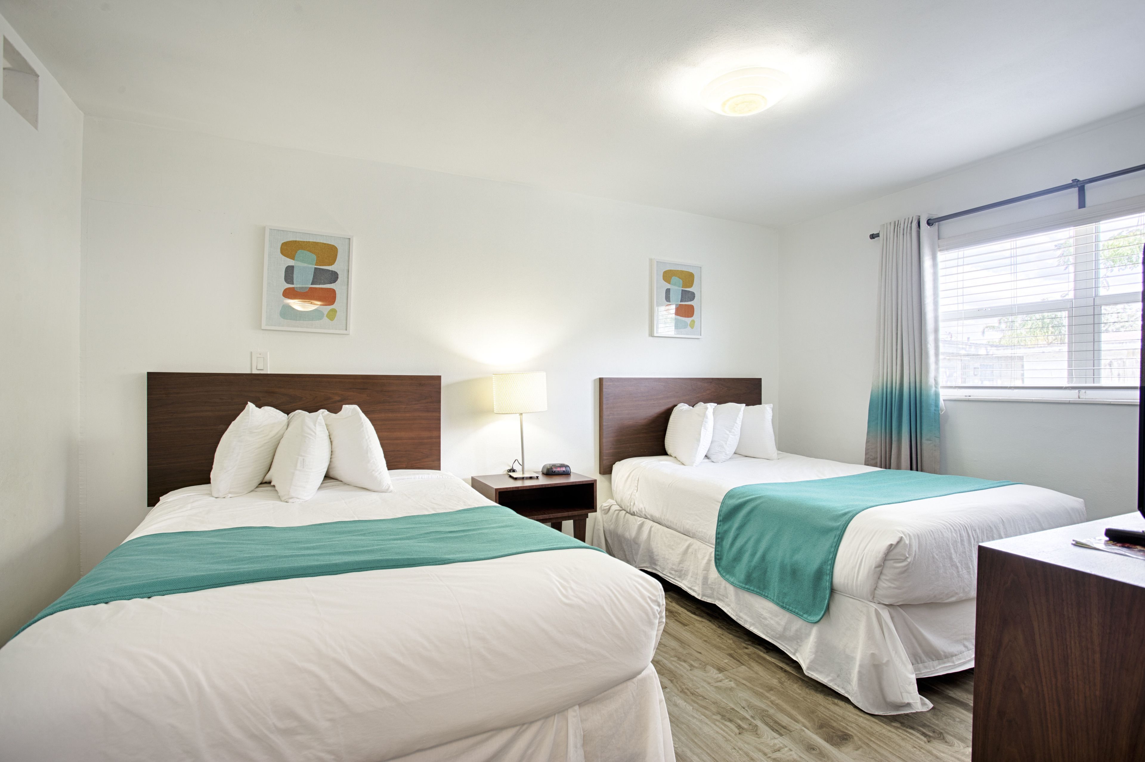 Habitación de hotel con dos camas, un escritorio y un ventanal con cortinas.