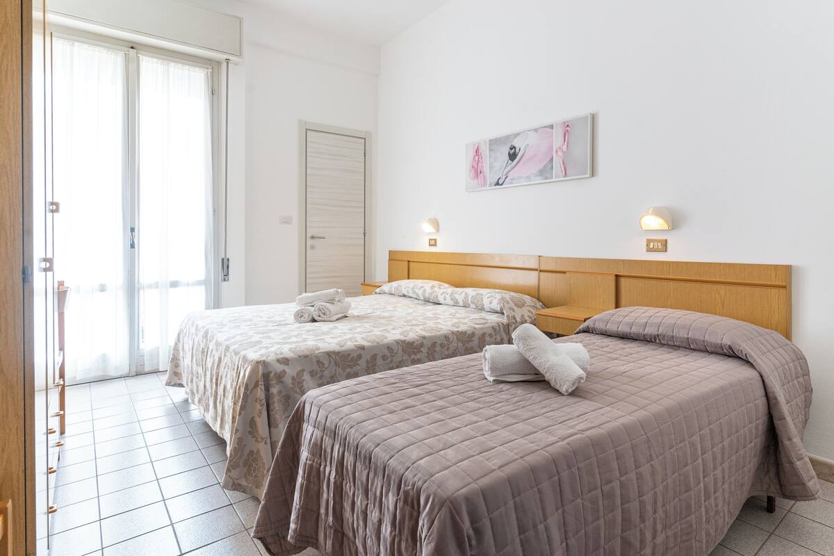 Habitación de hotel con dos camas, una puerta corrediza de vidrio, un cuadro en la pared y una lámpara de pared.