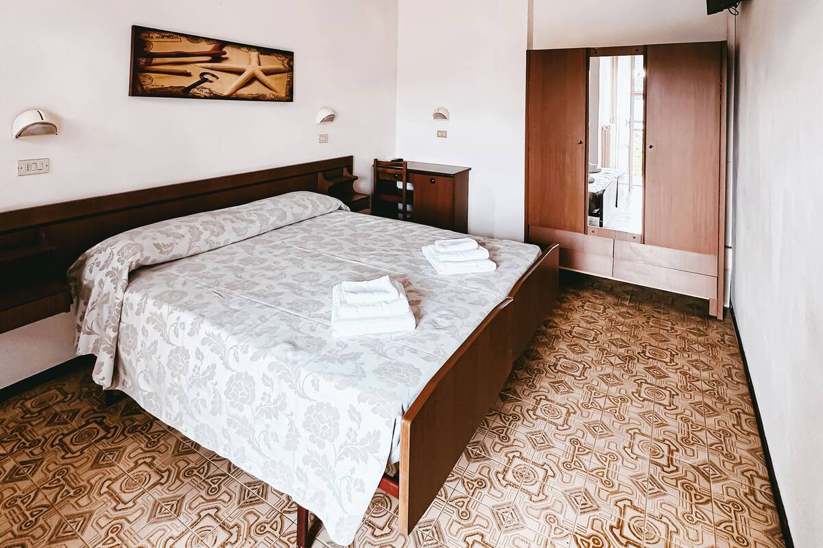 Un dormitorio con cama, mesitas de noche, televisión montada en la pared y suelo estampado.