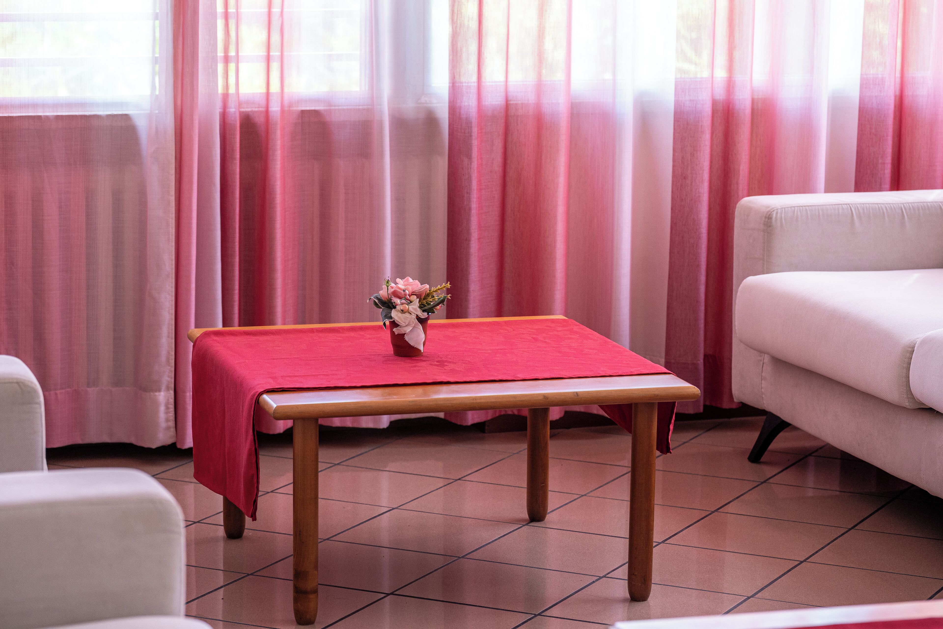 Una habitación con una mesa de madera cubierta por un mantel rojo, un sofá blanco y un jarrón con flores sobre la mesa.
