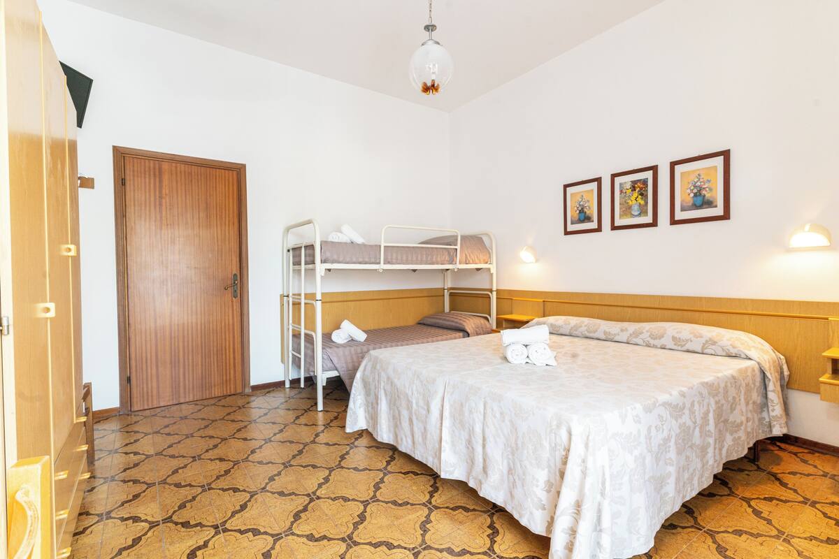 Una habitación con literas, una puerta de madera, baldosas de suelo estampadas y tres cuadros colgados en la pared.
