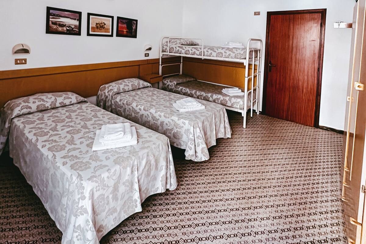 Habitación de hotel con dos camas individuales, una litera, una puerta de madera y un aire acondicionado de pared.