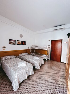 A hotel room with two single beds, a bunk bed, a wooden door, and a wall-mounted air conditioner. - Hotel Paglierani (San Mauro Pascoli)