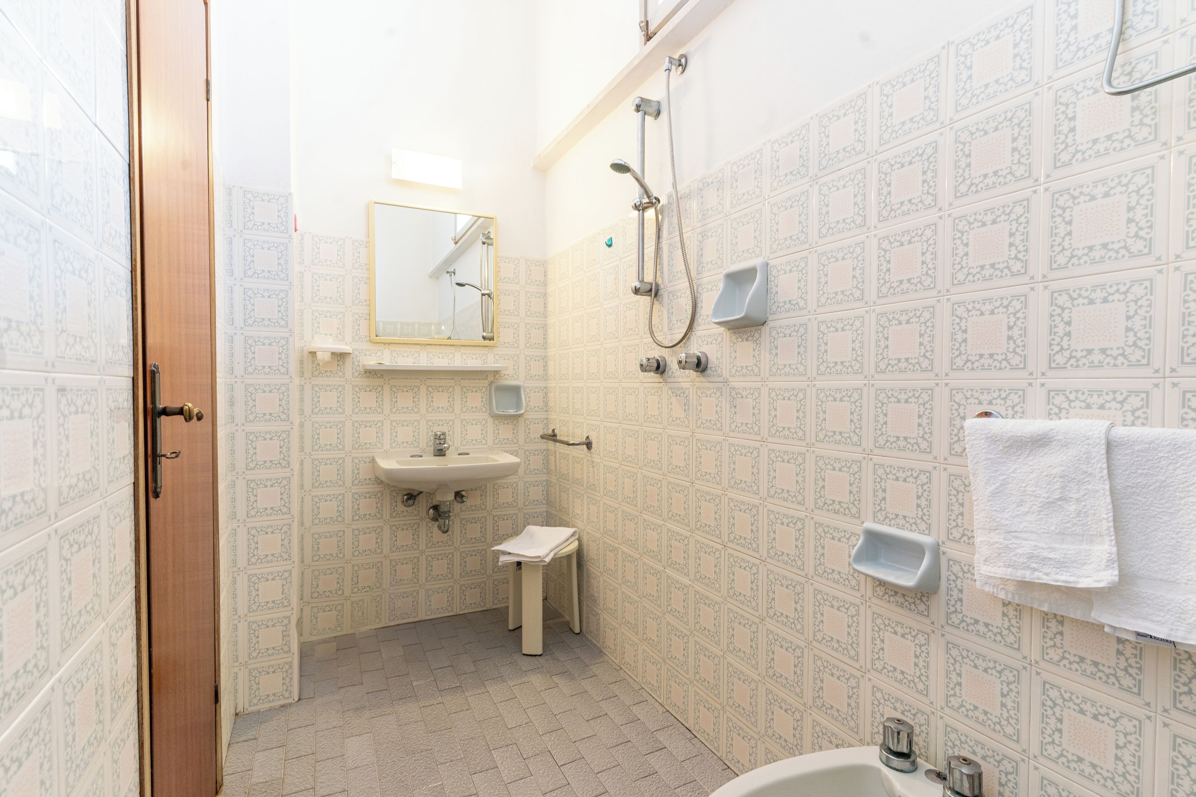 Une salle de bain avec des carreaux décorés, un lavabo, un miroir, une douche et un porte-serviettes.