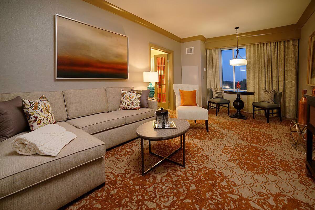 A hotel room with a sofa, armchairs, a coffee table, and a large painting on the wall.