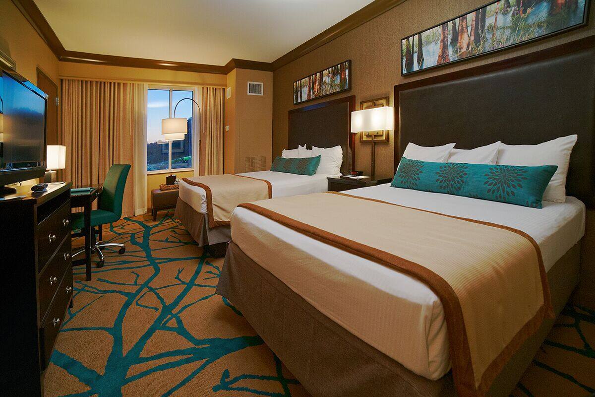 A hotel room with two beds, a desk with a TV, a chair, and a window with curtains.