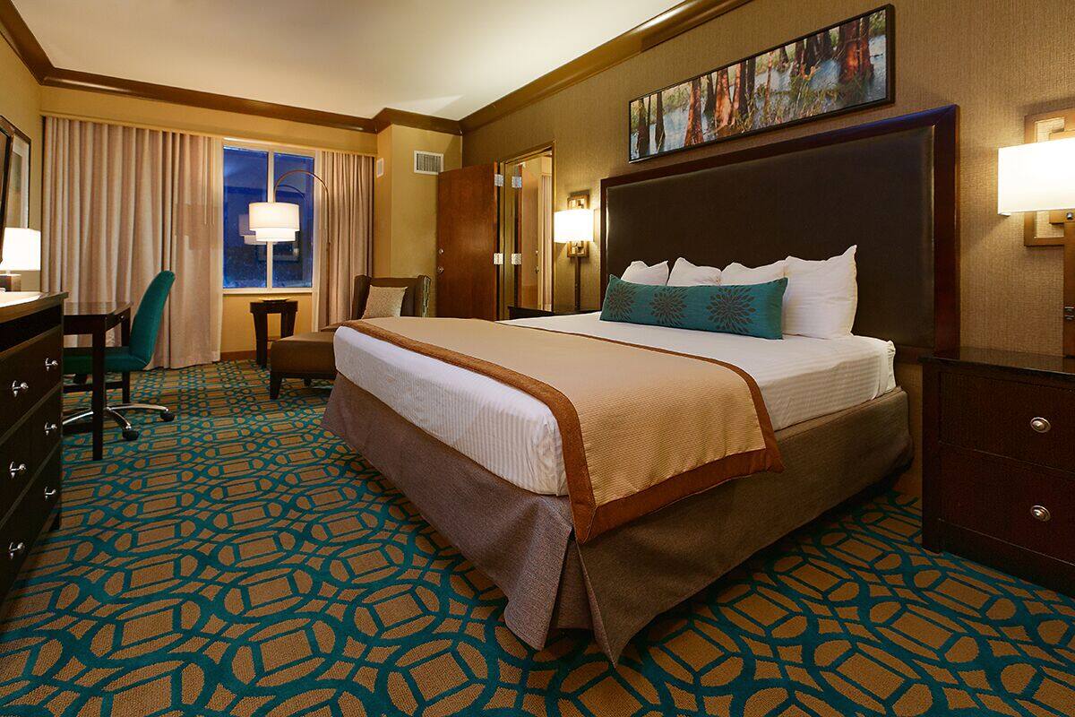 A hotel room with a large bed, a desk, a chair, a dresser, and a window with curtains.