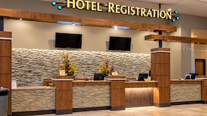 A hotel registration desk with a stone wall backdrop, wooden reception counters, and two flat-screen TVs mounted above the counters. - Riverwalk Casino Hotel (Vicksburg)