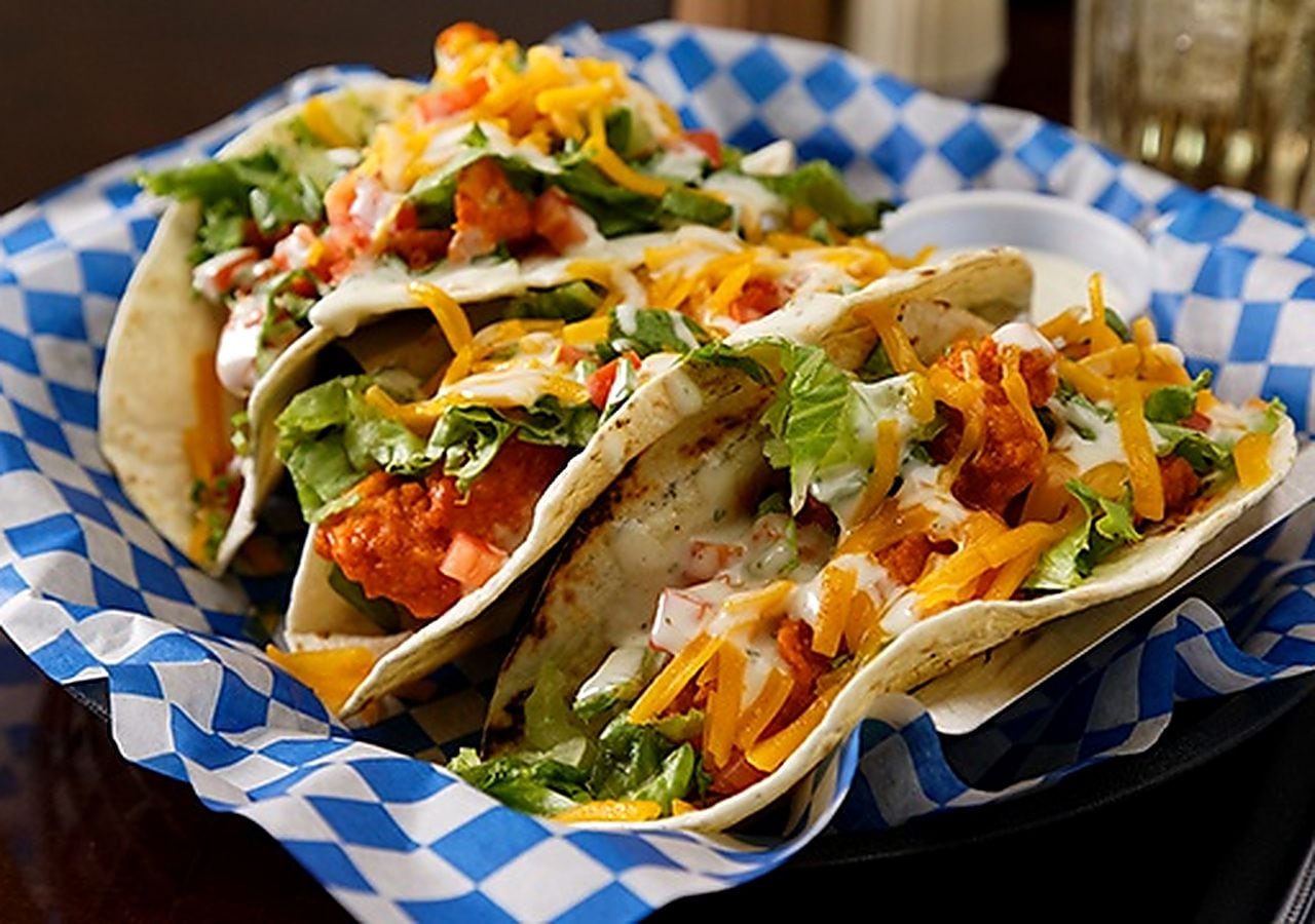 Trois tacos garnis de différentes sauces, présentés sur une serviette en papier à carreaux bleus et blancs.