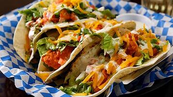 Trois tacos garnis de différentes sauces, présentés sur une serviette en papier à carreaux bleus et blancs.