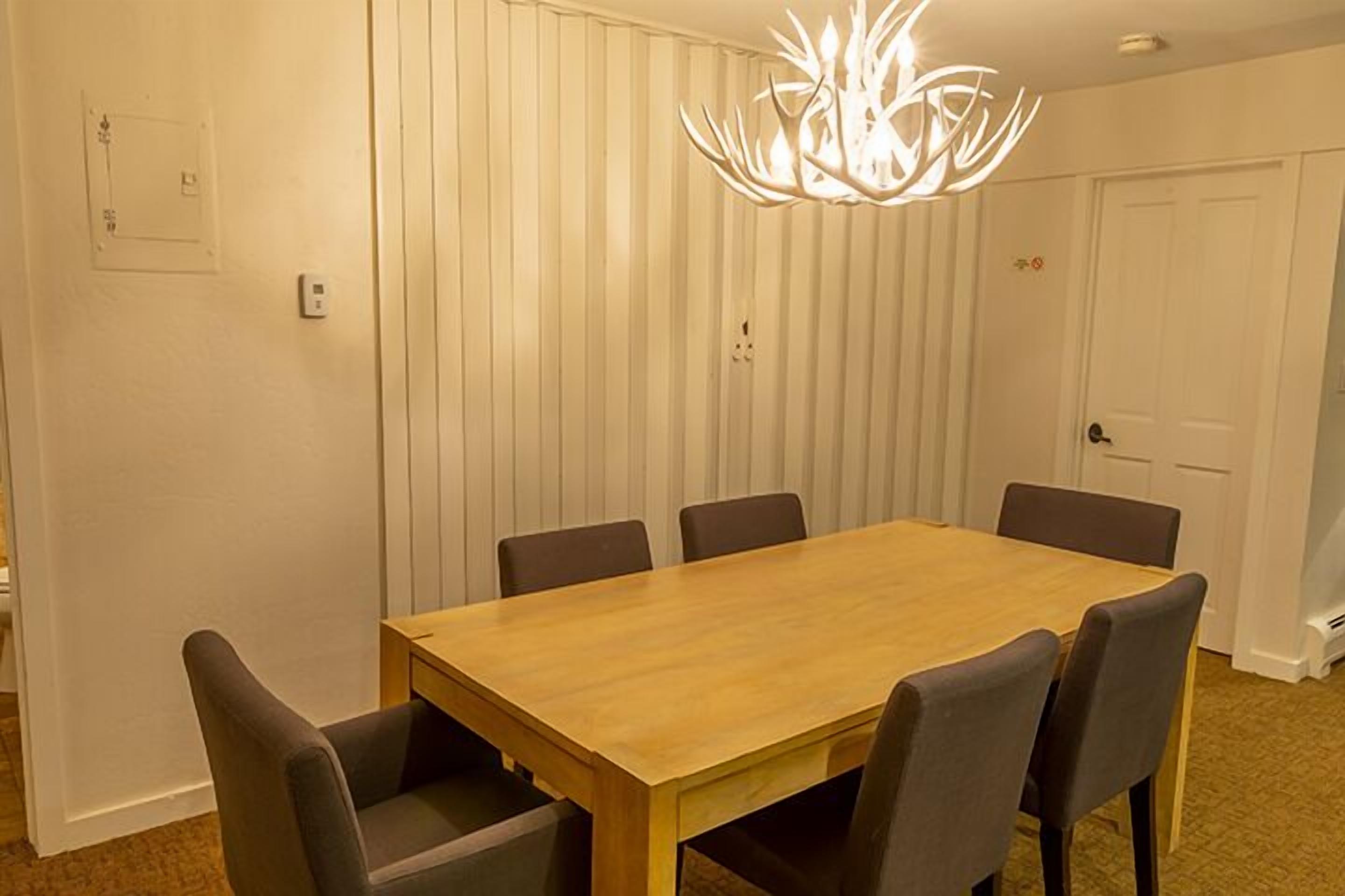 A dining area with a wooden table and six chairs, a chandelier, and a white door.