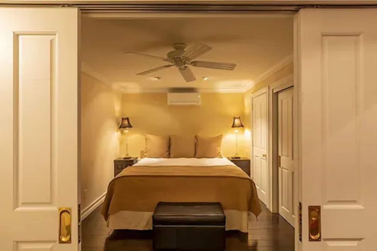Une chambre d’hôtel avec un lit, un ventilateur de plafond, des lampes de chevet et un banc.