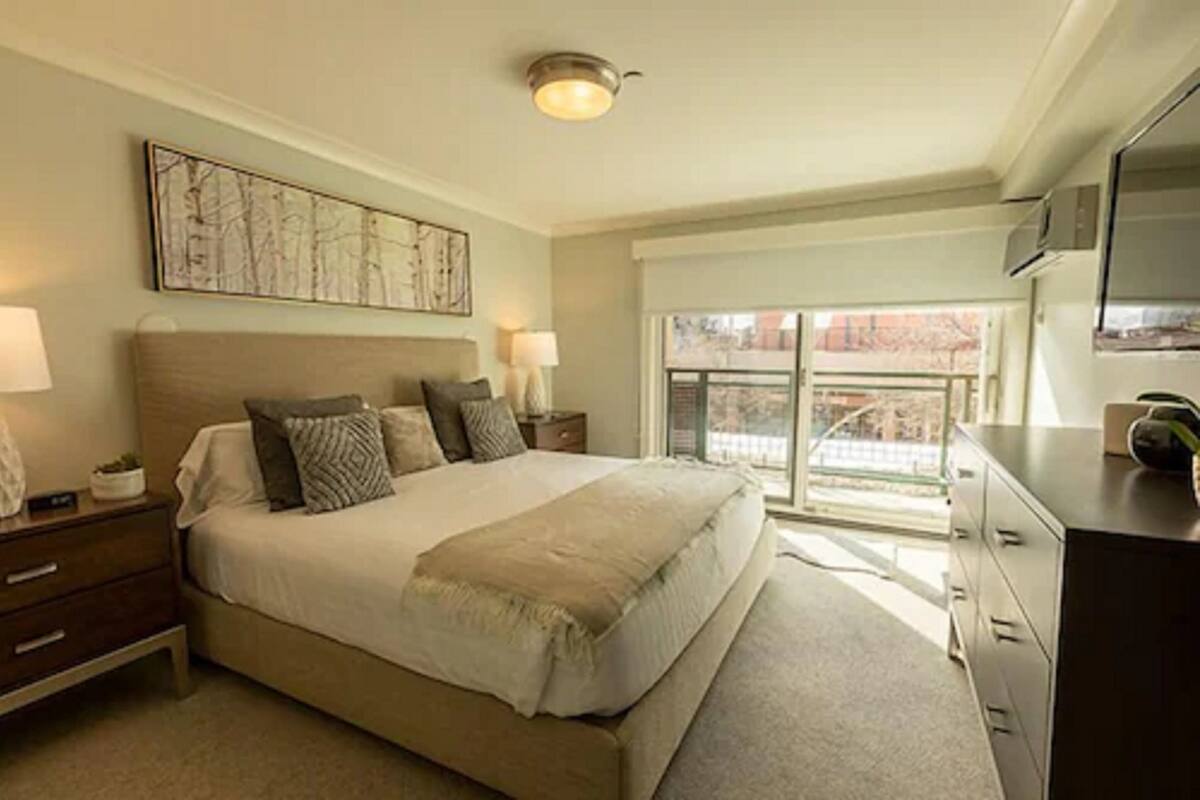 Une chambre à coucher avec un grand lit, deux tables de chevet avec des lampes, une commode et une grande fenêtre donnant sur un beau paysage.