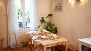 Une table à manger dressée avec des aliments pour le petit-déjeuner, entourée de chaises, dans une pièce dotée d’une fenêtre et d’une plante.