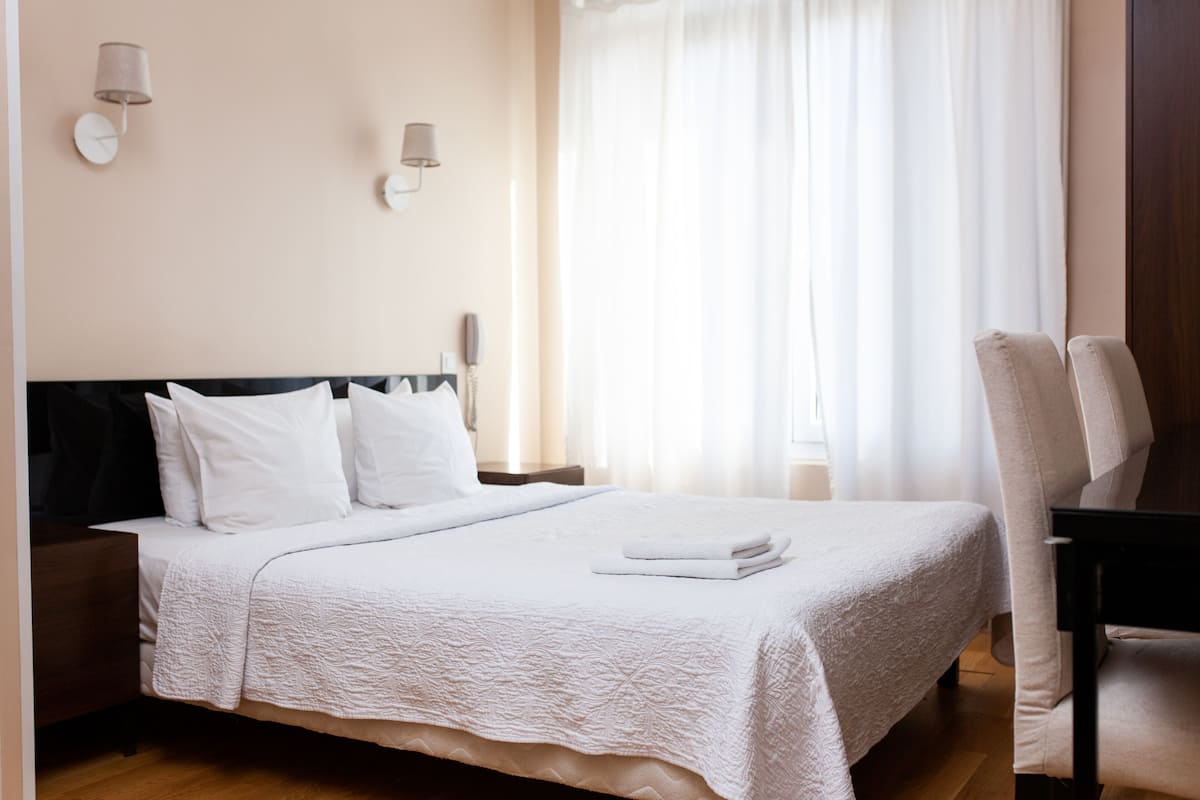 Ein ordentlich bezogenes Bett mit weißen Leinentüchern, einem hölzernen Kopfteil und einem Nachttisch mit einer Lampe.