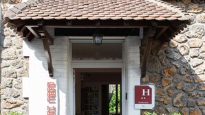 L’entrée d’un hôtel, avec un toit recouvert de tuiles, une façade en pierre et une enseigne indiquant un classement quatre étoiles.
